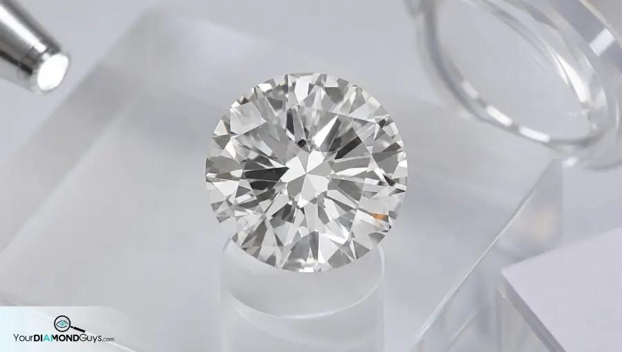 Round diamond on acrylic inspection pedestal showing laser drill channel and filled fracture flash clues
