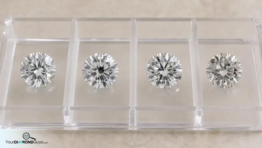 Four diamonds in acrylic lanes showing white center edge and multiple crystal inclusion checks