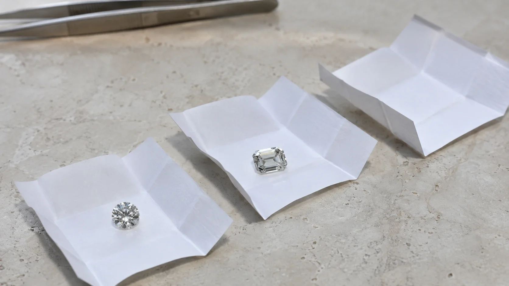 Round and emerald cut diamonds in separate open parcels beside an empty parcel