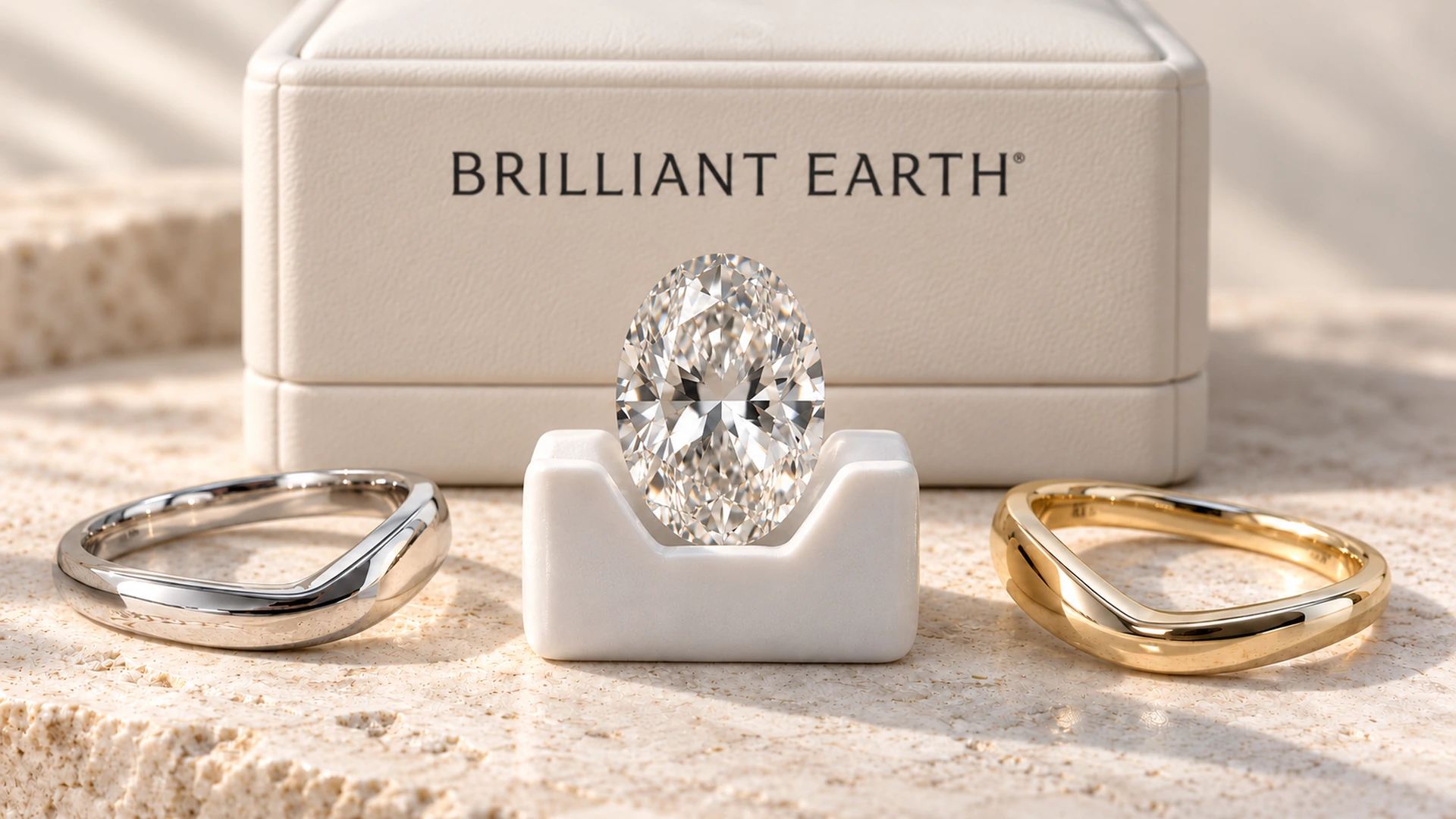 Oval diamond in a white ceramic cradle between platinum and gold bands, with the Brilliant Earth logo printed on an ivory presentation case behind it