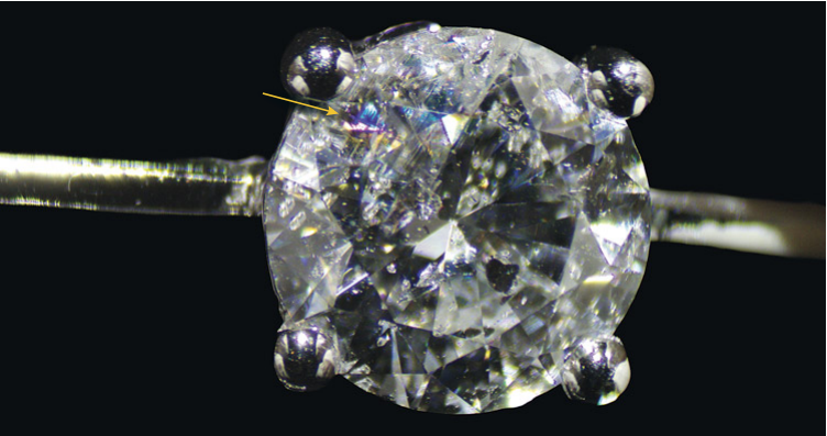 GIA photograph of a mounted round diamond with an arrow marking the fracture filling flash effect